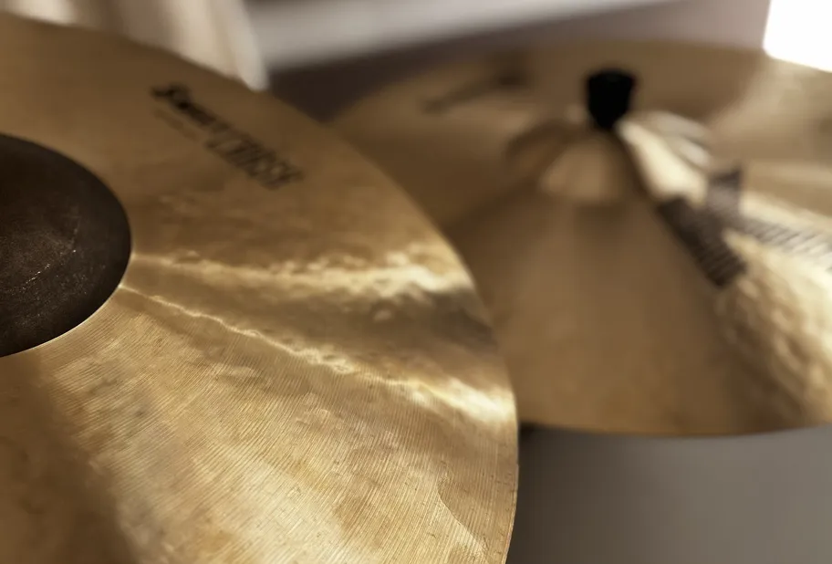 Plusieurs cymbales de batterie sur fond sombre, reflétant la lumière.